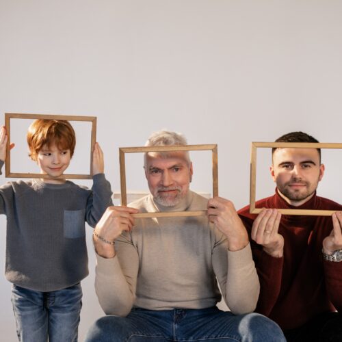A couple with their son, all holding picture frames around their faces.