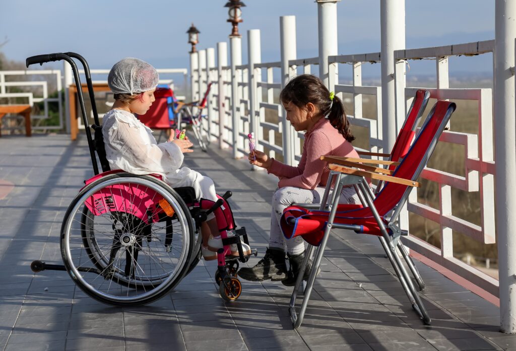 Girl in a Wheelchair on a dock, sitting across from girl in a chair